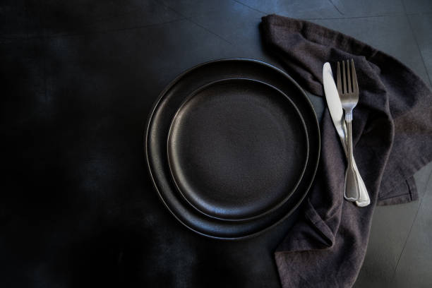 istock Black plate, cutlery and napkin on dark table 1305849393