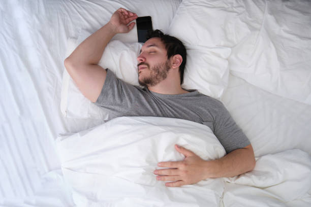 istock Young latin man sleeping spread out in bed with his smartphone. Sleep position concept. 1305853235