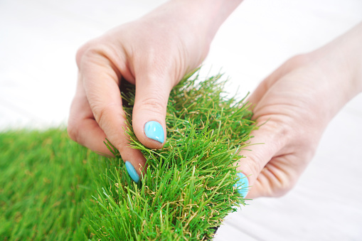 Tender female hand touching soft artificial grass roll