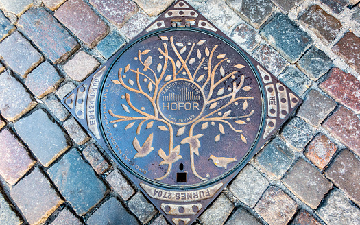 Copenhagen, Denmark - Oct 19, 2018: Ornate utilities company, HOFOR, manhole heavy gauge metal cover along a street. The company supplies water, sanitation, district town gas and cooling.