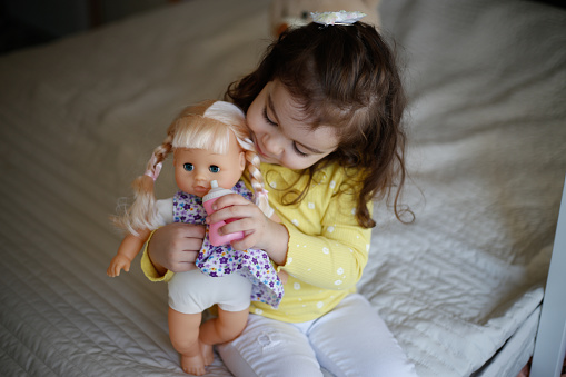 Young girl pretends play babysitting with baby doll at home.