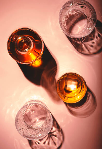 zeitgenössisches stillleben mit whiskey, scotch oder bourbon glas mit eis auf strukturiertem rosa hintergrund mit harten lichtern und schatten, ansicht von oben, kopierraum - distillery still stock-fotos und bilder
