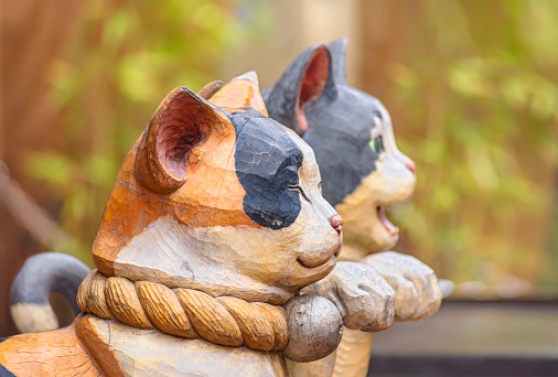tokyo, japan - february 28 2021: Profile view of an aum pair of wooden closed-mouthed and open-mouthed statues depicting Japanese maneki-neko cats with a paw raised in the Yanaka-Ginza shopping street.