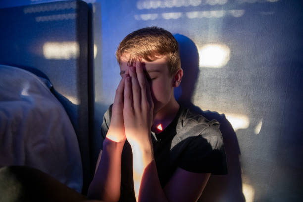 stressed out teenager boy sitting in a dark room, with light spots coming though the window.