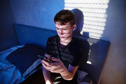 teenager boy sitting in his bedroom using cell phone