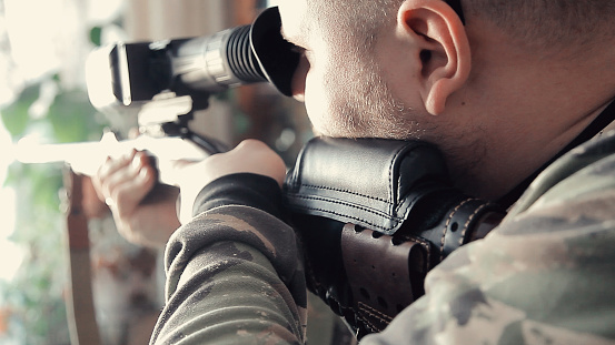 A man with a gun is aiming and looking at the sight. The carbine is aimed to prepare for a firearm shot. Man in camouflage clothing.