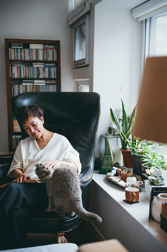 Senior Asian woman enjoying her time with pet while reading book.