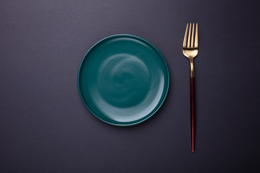 Empty green plate and fork on black  background. Top view.