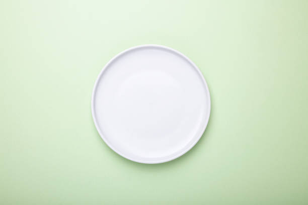 istock Empty white plate on green background with clipping Path. Top view. 1305877276
