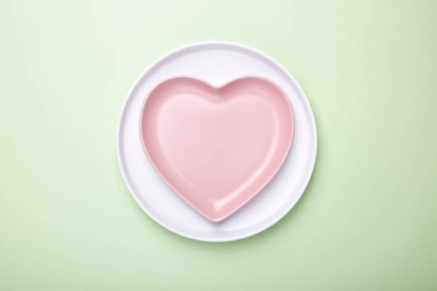 Empty white plate and pink heart-shaped plate on pink background with clipping Path. Top view.