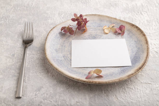 istock White paper invitation card, mockup with dried hydrangea flowers on ceramic plate and gray concrete background. Blank, side view, still life, copy space. 1305881516