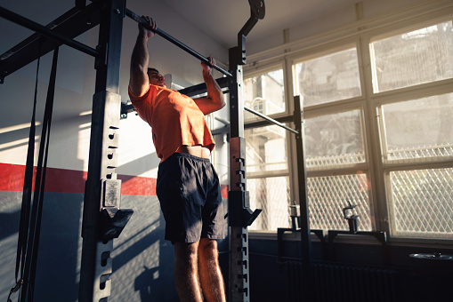 Young man doing pull-ups in a gym.