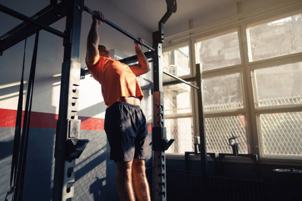 Young man doing pull-ups in a gym Young man doing pull-ups in a gym. chin ups stock pictures, royalty-free photos & images