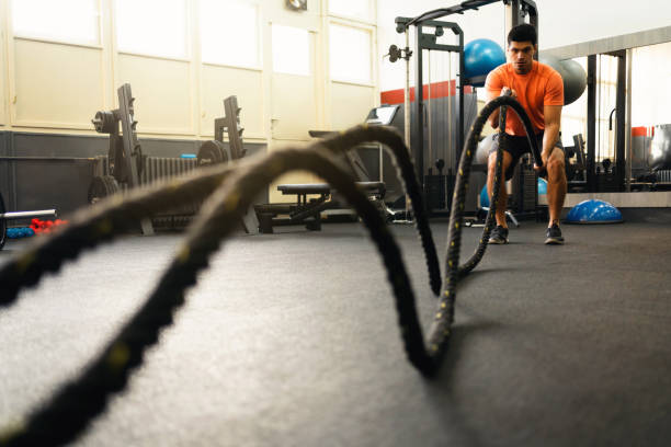 istock Young man doing battle rope squatting alternating waves in gym 1305883538