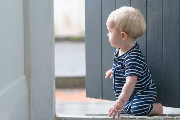 il bambino guarda una pioggia dalla porta sul retro di casa sua - looking at camera full length outdoors image technique foto e immagini stock
