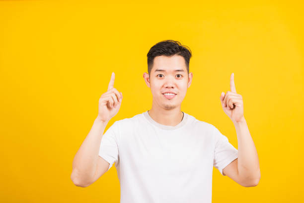 istock young man smiling standing pointing finger to above UP side 1305897835