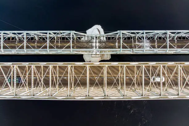 Two old iron bridges crossing the river. The steel structures are covered in frost and the small island below them has a snow cover.