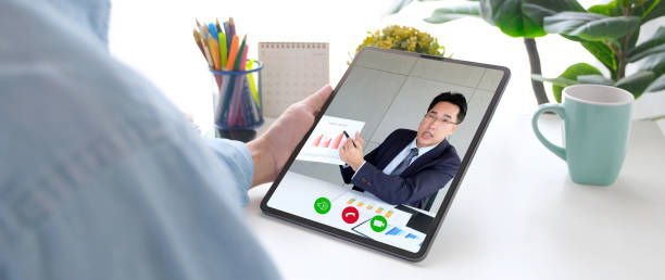 istock Video conference, Work from home, Asian man holding business chart on digital tablet while making video call to business team with virtual web, Contacting colleague by conference at home 1305904593