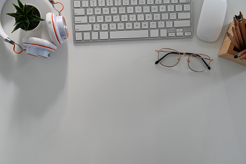 Above view of office desk with keyboard, glasses, headphone and copy space on white background.