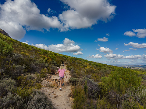 Rear wide view of Young blond girl hiking in the mountains between fynbos vegetation Stellenbosch South Africa