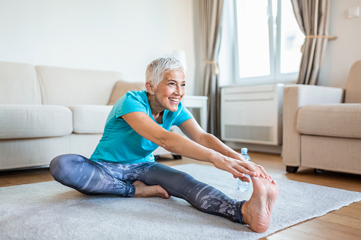Senior woman doing warmup workout at home. Fitness woman doing stretch exercise stretching her legs,quadriceps .Elderly woman living an active lifestyle.