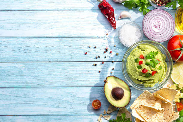 ciotola di guacamole e nachos con ingredienti su sfondo blu. con spazio di copia. vista dall'alto. - light vegetarian food garlic spice foto e immagini stock