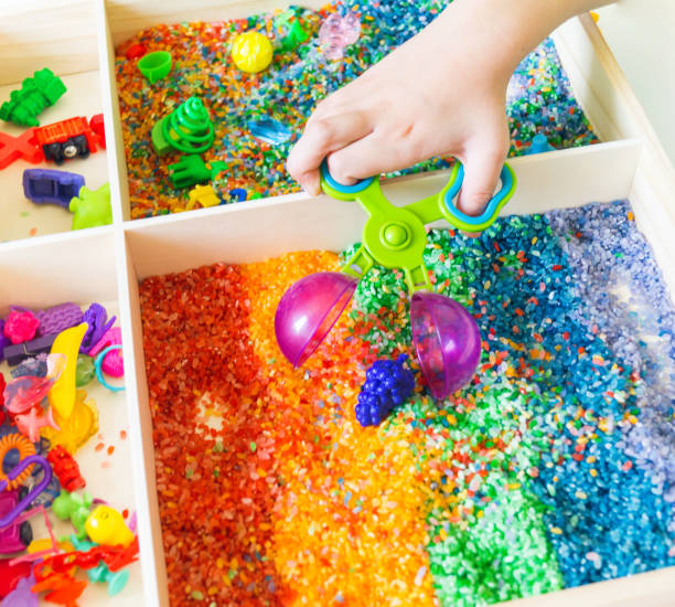 istock Sensory box with rainbow rice inside. Montessori material baby 1305914965