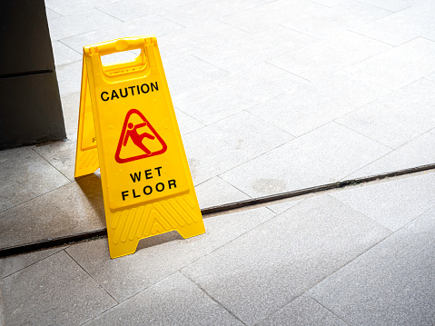 Mature Man Falling On Wet Floor In Front Of Caution Sign At Office