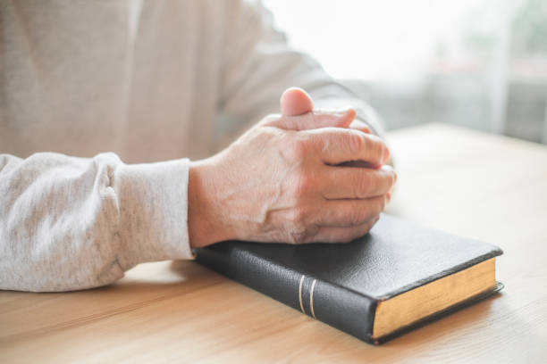 istock senior man praying, reading  an old Bible in his hands. 1305920698