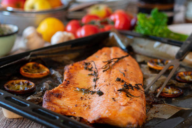 grilled fish fillet on a baking sheet homemade mediterranean fish fillet with wild salmon grilled in the oven with herbs and lemon slices. whole and halved. ready to eat Baked Salmon stock pictures, royalty-free photos & images
