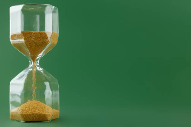 istock Gold hourglass on dark green paper background 1305923003