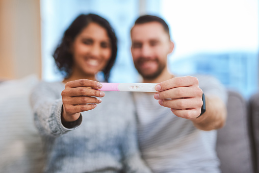 Cropped shot of an unrecognizable couple sitting on the sofa together and holding a positive pregnancy test