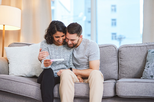 Cropped shot of a happy young couple sitting on the sofa together and holding a positive pregnancy test