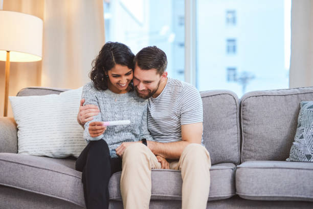 I can't wait for the results! Cropped shot of a happy young couple sitting on the sofa together and holding a positive pregnancy test pregnancy test stock pictures, royalty-free photos & images