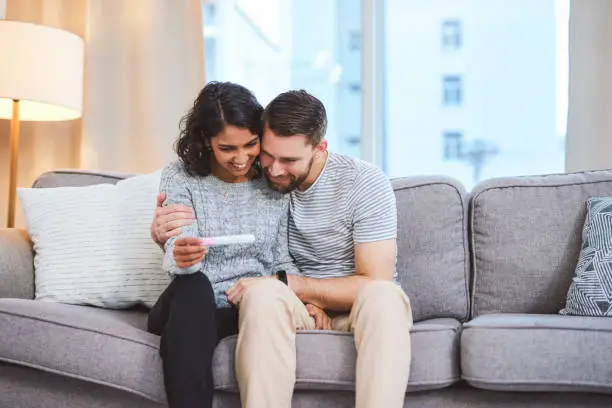 Cropped shot of a happy young couple sitting on the sofa together and holding a positive pregnancy test