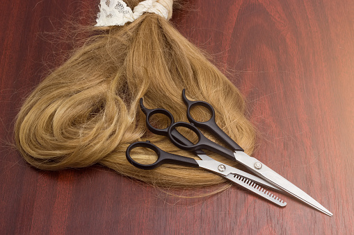 Normal hairdressers scissors and thinning shears lie on a strand of light brown female hair on a wooden table