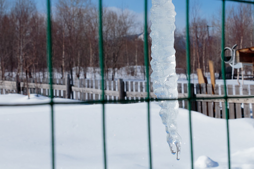 A lonely icicle melting in the sun hanging from the roof.