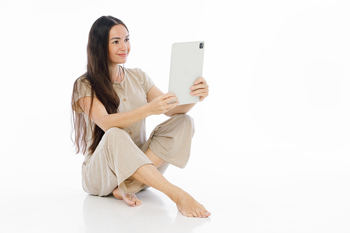 Young brunette woman siting on floor, work on tablet computer or make photo. Lifestyle concept on white background.