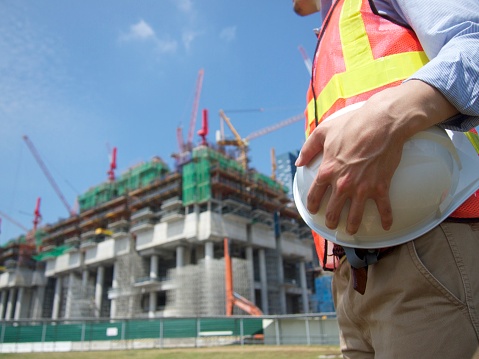 A builder is standing with a helmet in front of a building under construction in Singapore.
