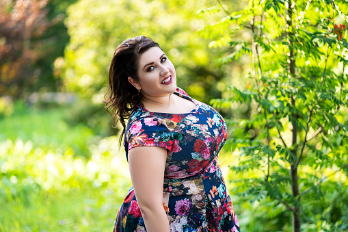 Happy plus size model in floral dress outdoors, beautiful fat woman in nature, body positive concept