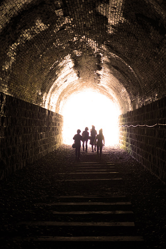 People walking with hope towards the light in a tunnel of a discontinued train line.