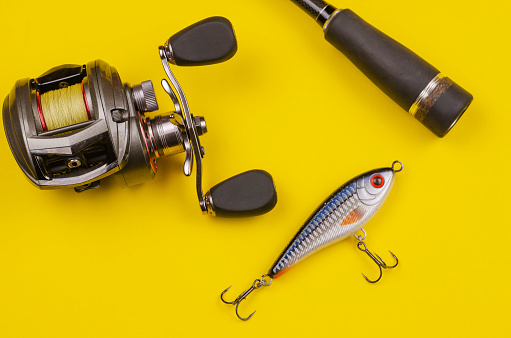 Fishing tackle for predatory fish. Fishing rod with reel and bait on yellow background. Casting rod with a multiplier reel and fishing line. Artificial bait. Selective focus.