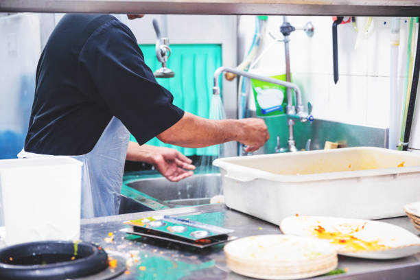Restaurant Dish Washing Staff at Work Dish washing staff at a restaurant rinsing and cleaning the dirty plates minimum wage stock pictures, royalty-free photos & images