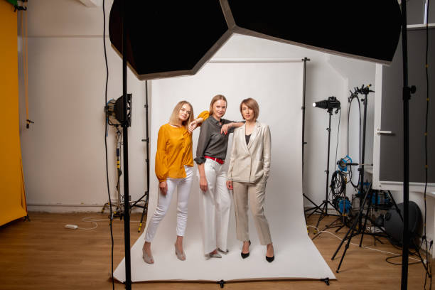 shooting backstage professional photography women Shooting backstage. Professional photography. Female team. Creative work. Confident business women posing on white background in modern studio with light equipment. photo studio model stock pictures, royalty-free photos & images