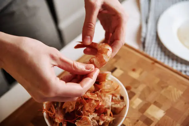 Photo of Woman cleaning shrimps for cooking. Process of hands peel shrimps shell