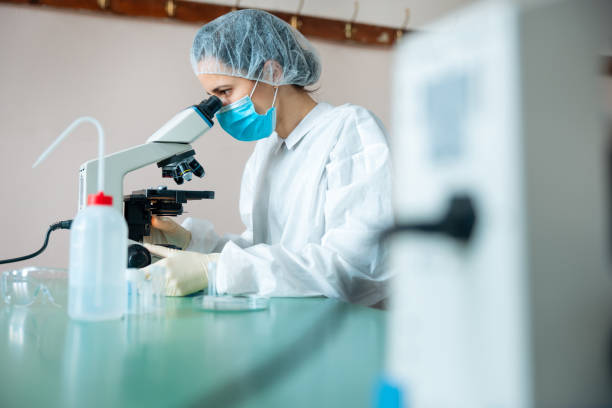 istock Female scientist in protective headwear, mask and gloves working in microscopy lab 1305942329