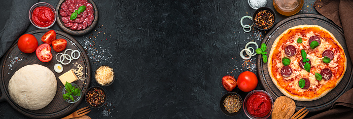 Raw ingredients and ready-made pizza on a black background. Banner with copy space, Cooking background.