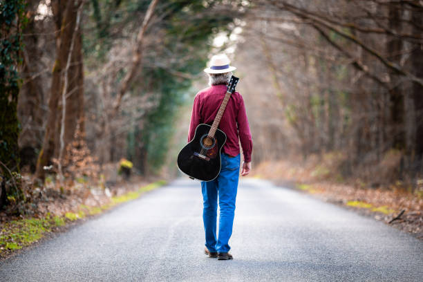 istock Free wandering man walking on country road with guitar on his back 1305946292