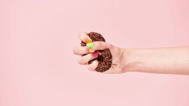 istock Female hand squeezing chocolate donut on pink background 1305946295