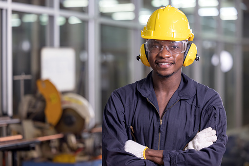 Retrato de un alegre trabajador negro con auriculares protectores posando mirando la cámara y disfrutando del trabajo en la fábrica de fondos photo